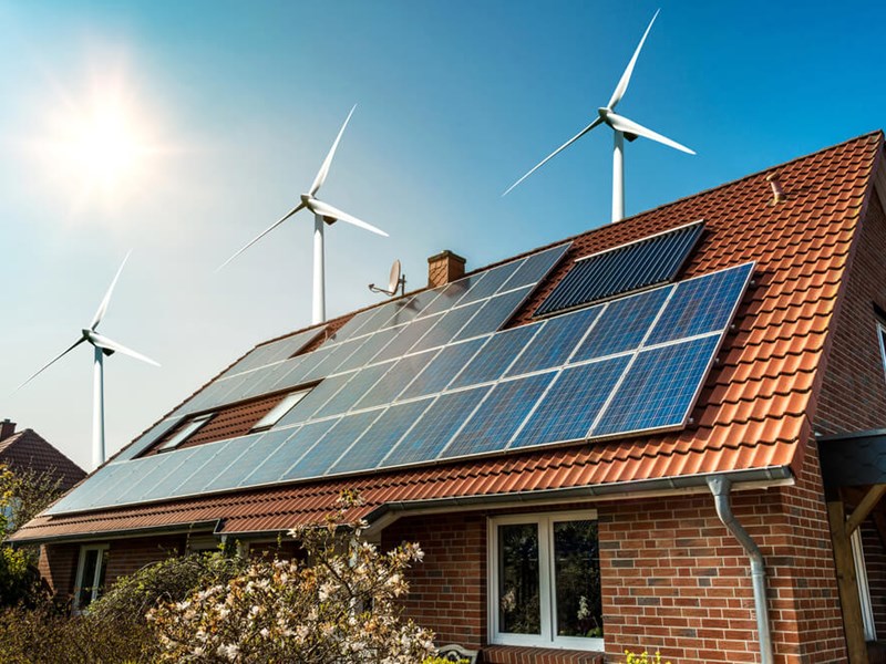 Home with solar panels with wind turbines behind